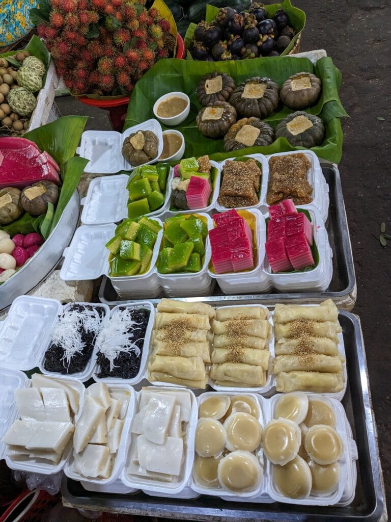 Traditional Cambodian Desserts at Kampot Market Assorted Cambodian desserts and fruits displayed at a market stall in Kampot.