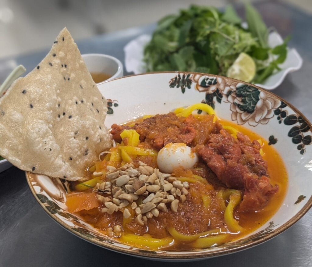 Bowl of Mì Quảng served with fresh herbs in Đà Lạt