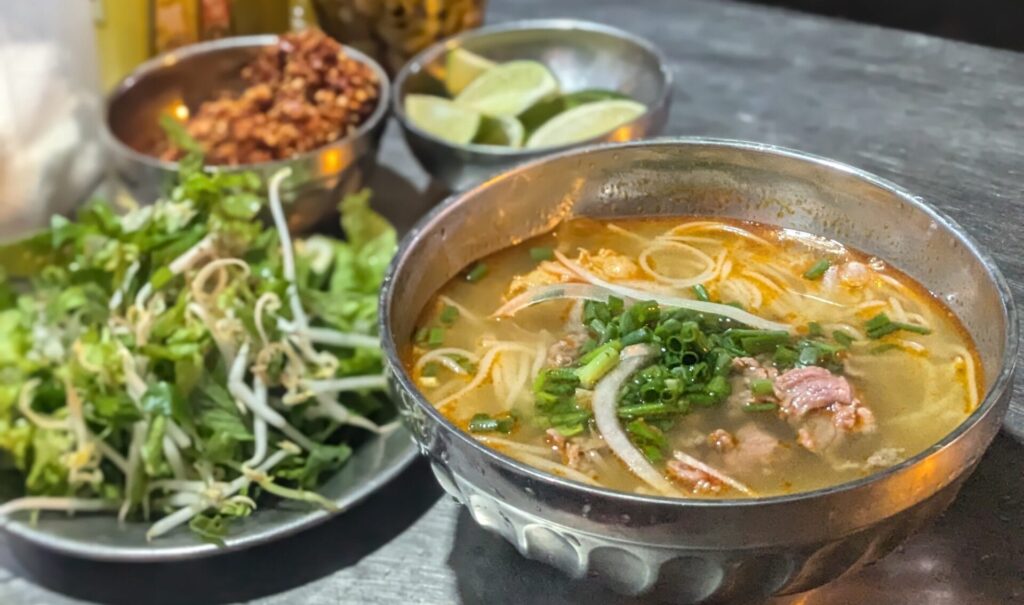 Bowl of Bún bò Huế noodle soup with beef and herbs