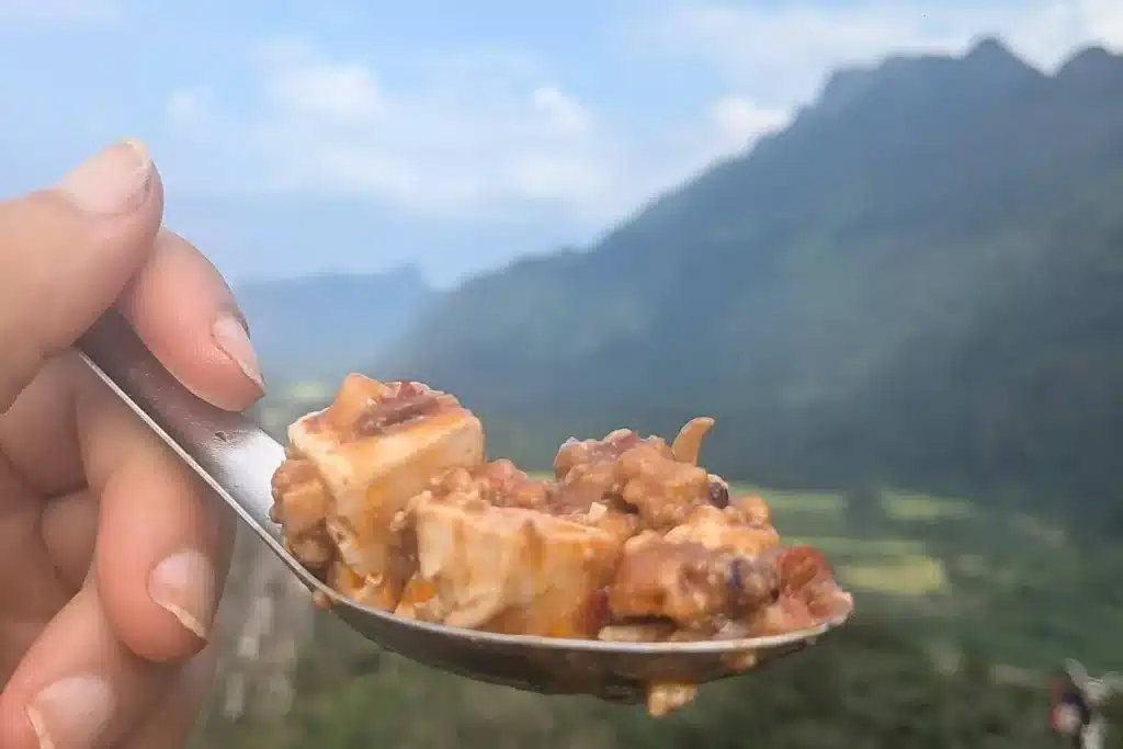 Mapo Tofu and Mountain Views Spoonful of spicy mapo tofu held against the backdrop of Vang Vieng’s limestone mountains.