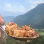 Spoonful of spicy mapo tofu held against the backdrop of Vang Vieng’s limestone mountains.